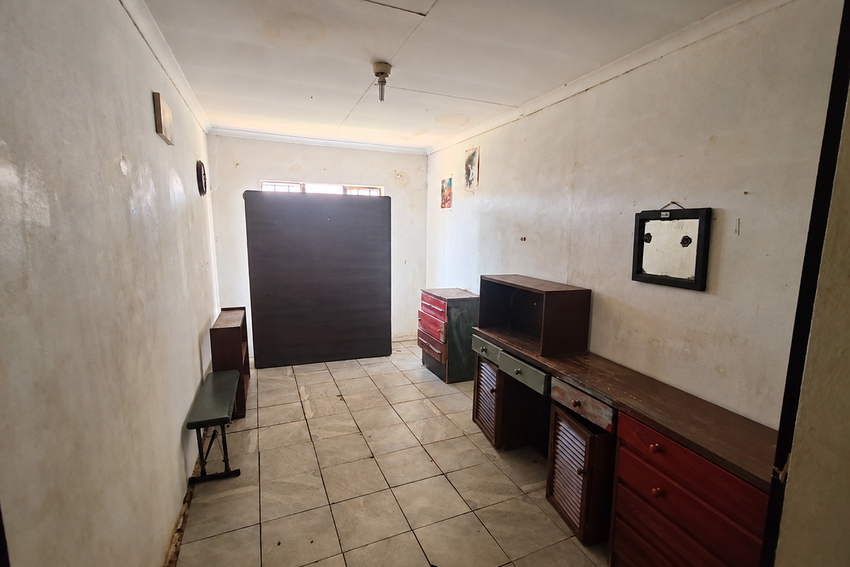 A bedroom featuring tiled flooring and dated wall finishes, requiring cosmetic updates and repairs to the flooring and walls.