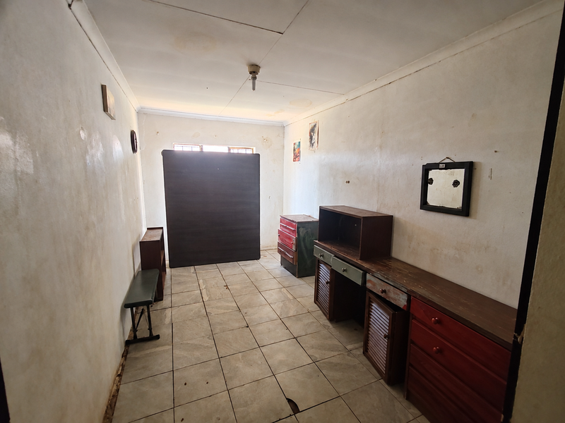 A bedroom featuring tiled flooring and dated wall finishes, requiring cosmetic updates and repairs to the flooring and walls.