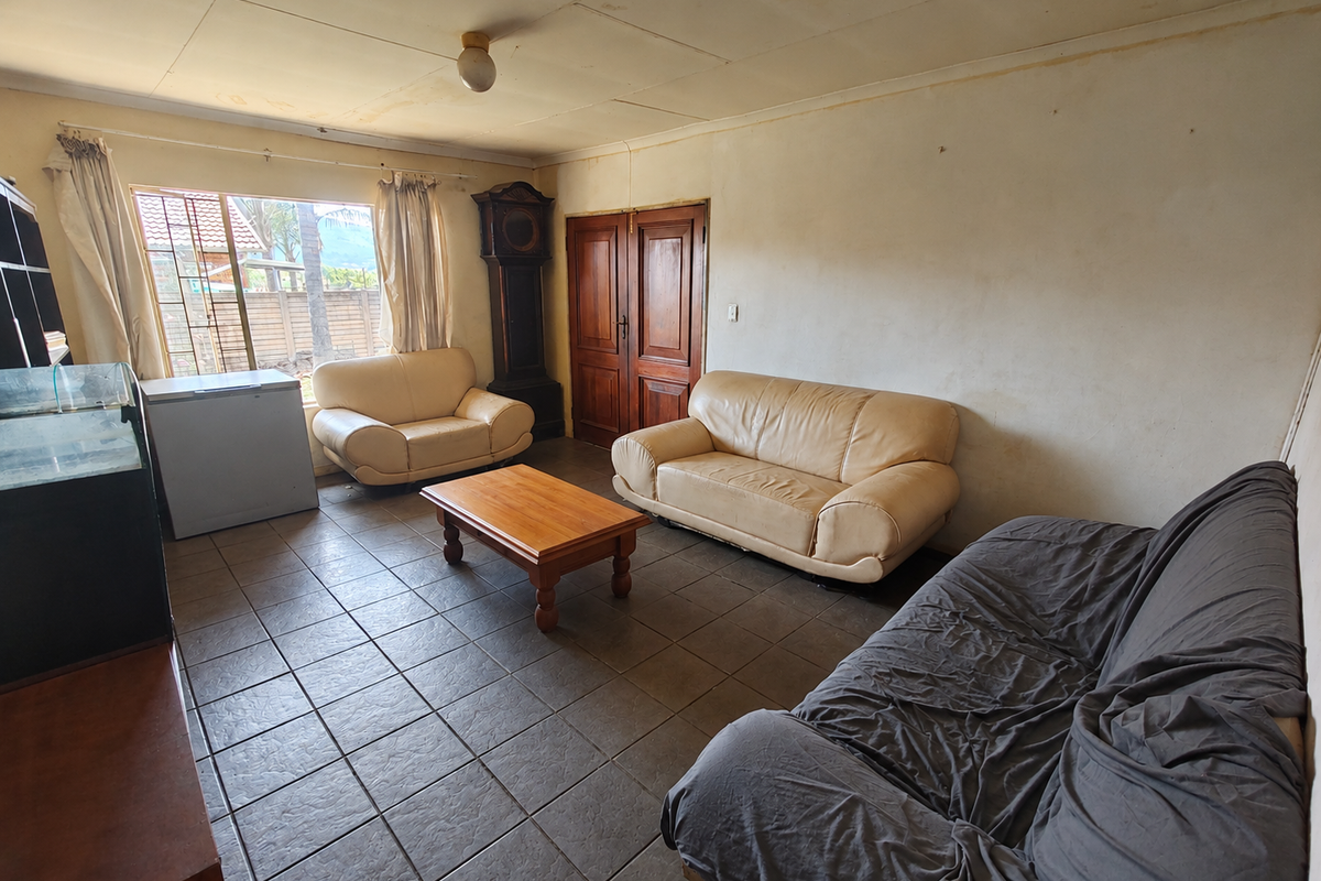 A living room featuring tiled flooring, double wooden doors, and a large window, currently showing signs of wear on the walls and ceiling.