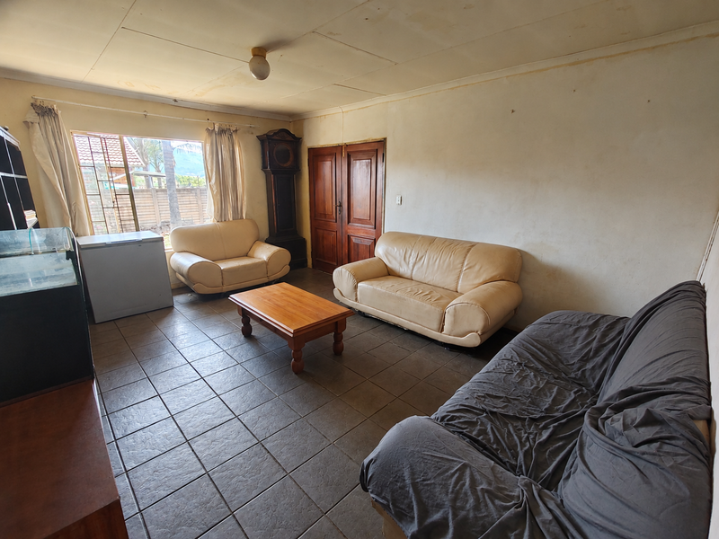 A living room featuring tiled flooring, double wooden doors, and a large window, currently showing signs of wear on the walls and ceiling.