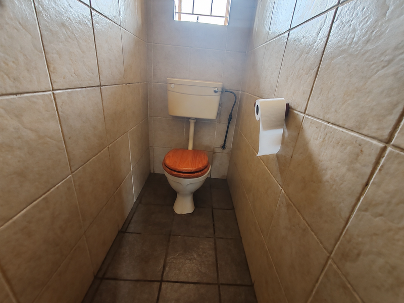 A compact, tiled bathroom featuring a standard toilet and cistern, with a small high-level window providing natural light.