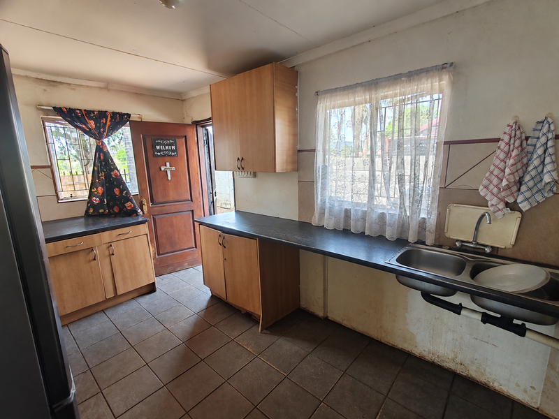 A functional kitchen featuring laminate cabinetry, a double bowl stainless steel sink, and tiled flooring, with direct access to an exterior door.