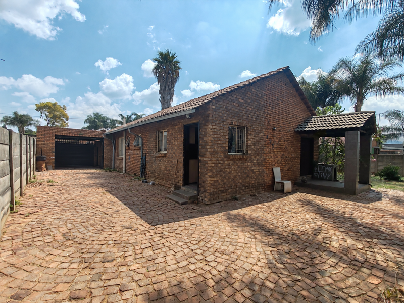 A detached face brick house featuring a paved driveway, a single garage, and a covered entrance area, set within a fenced property.