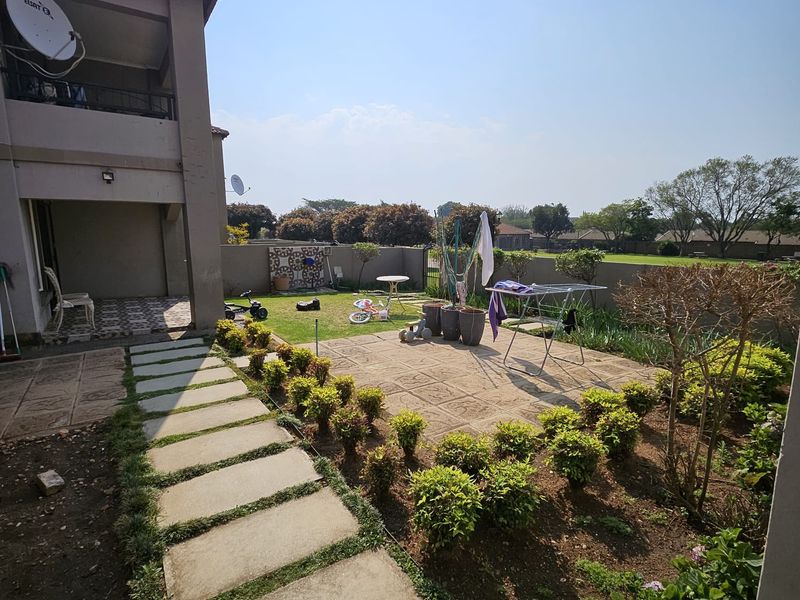 Rear exterior view of a townhouse featuring a paved patio area, covered terrace, and a garden with concrete stepping stones and boundary wall.