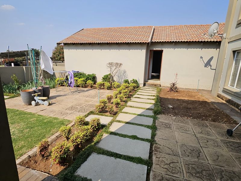 A rear exterior view of the townhouse featuring a paved patio area, concrete stepping stones, and a small garden space with a tiled roof structure.