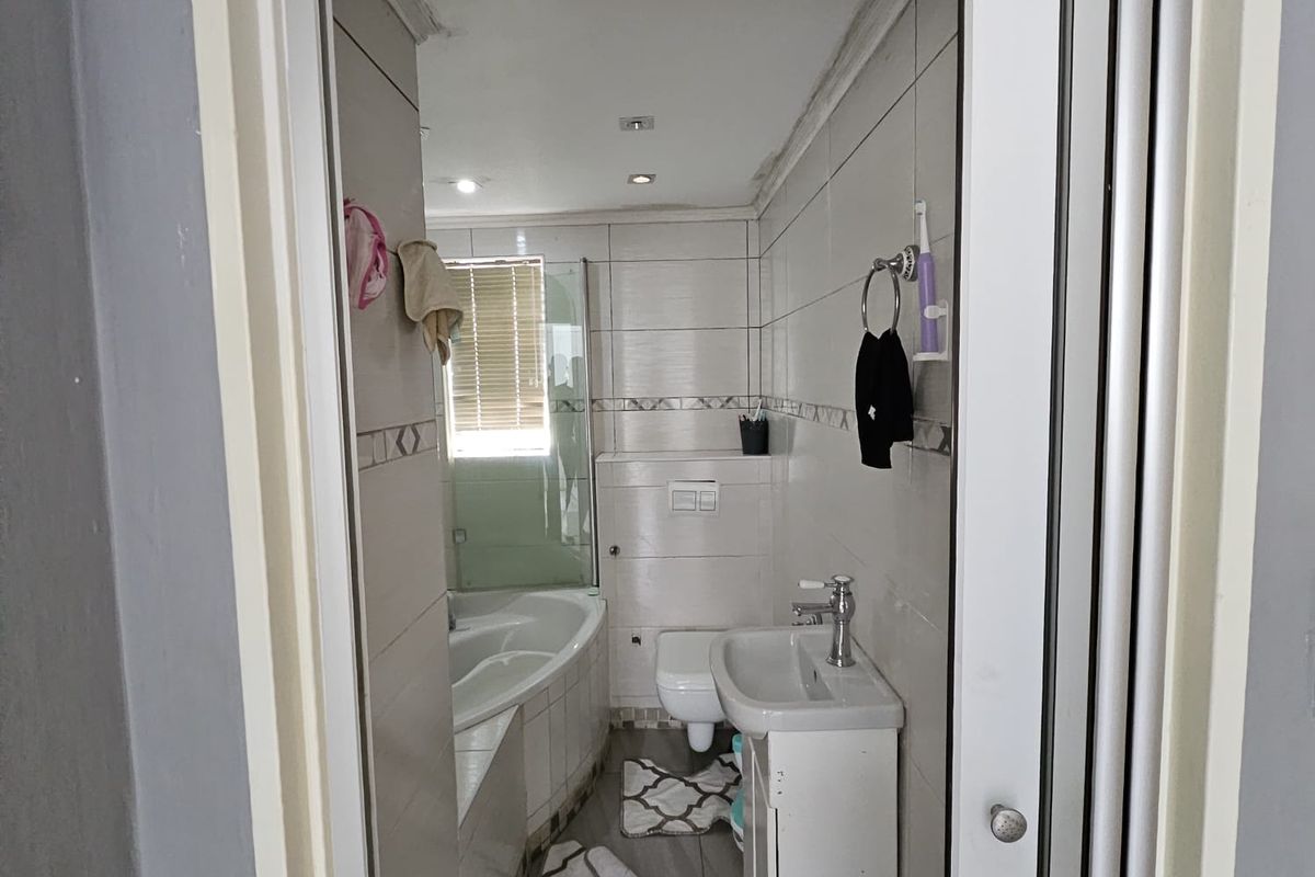 A compact bathroom featuring a built-in bathtub, wall-hung toilet, and vanity basin with tiled finishes throughout.