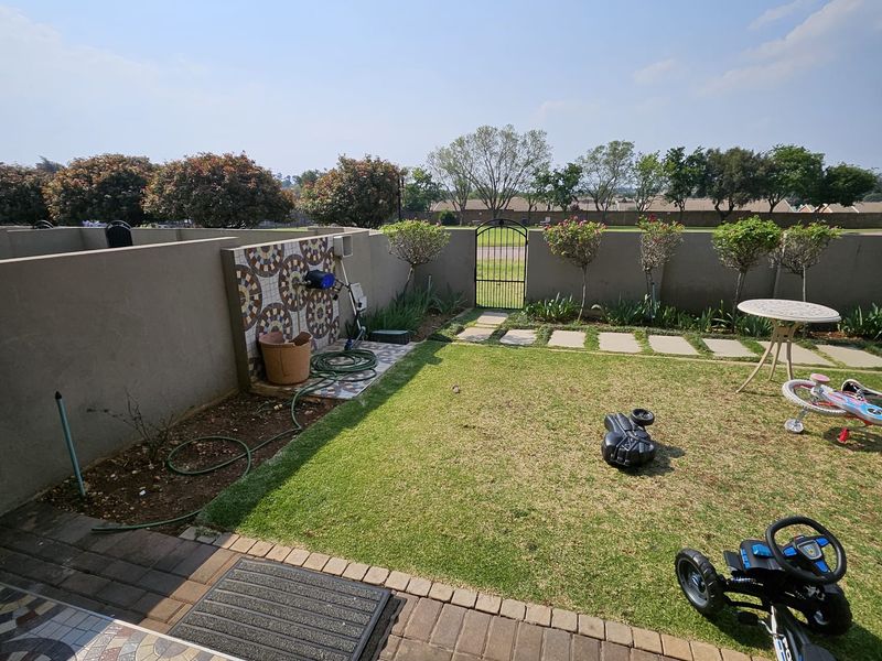 A private rear garden featuring a paved patio, a decorative mosaic feature wall, a lawn area, and a metal gate leading to the estate grounds.
