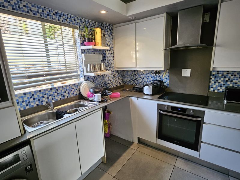 Functional kitchen featuring white cabinetry, stainless steel appliances, a tiled mosaic splashback, and large floor tiles.