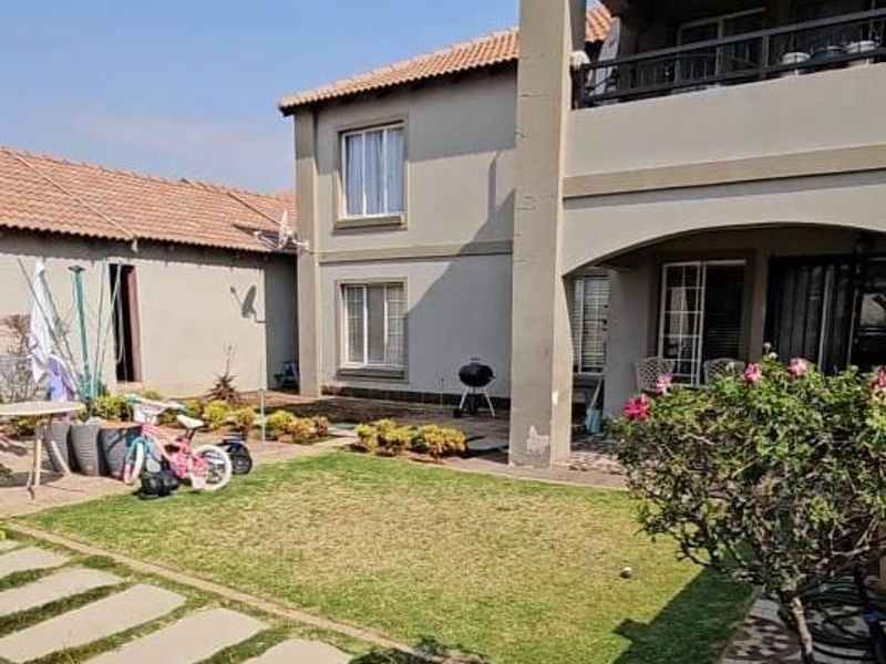Rear view of a two-story townhouse featuring a covered patio, upper balcony, small lawn, and paved walkway.