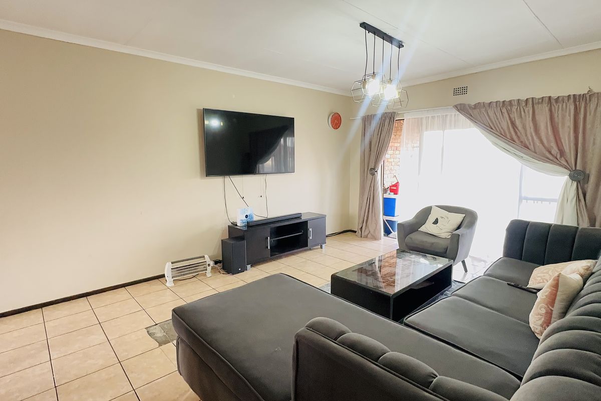 A living room featuring tiled flooring, a coved ceiling, and a sliding glass door providing access to the outdoor area.