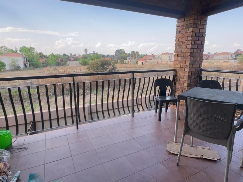 A covered balcony featuring tiled flooring, brick support columns, and a metal balustrade, offering an open view of the surrounding neighborhood.