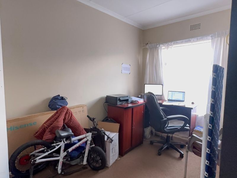 A bedroom space featuring carpet flooring and a window, currently utilized as a home office area.