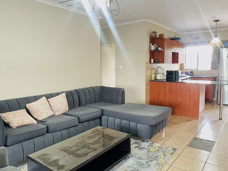 Open-plan living area featuring a kitchen with wooden cabinetry and tiled flooring, seamlessly connecting to the lounge space.
