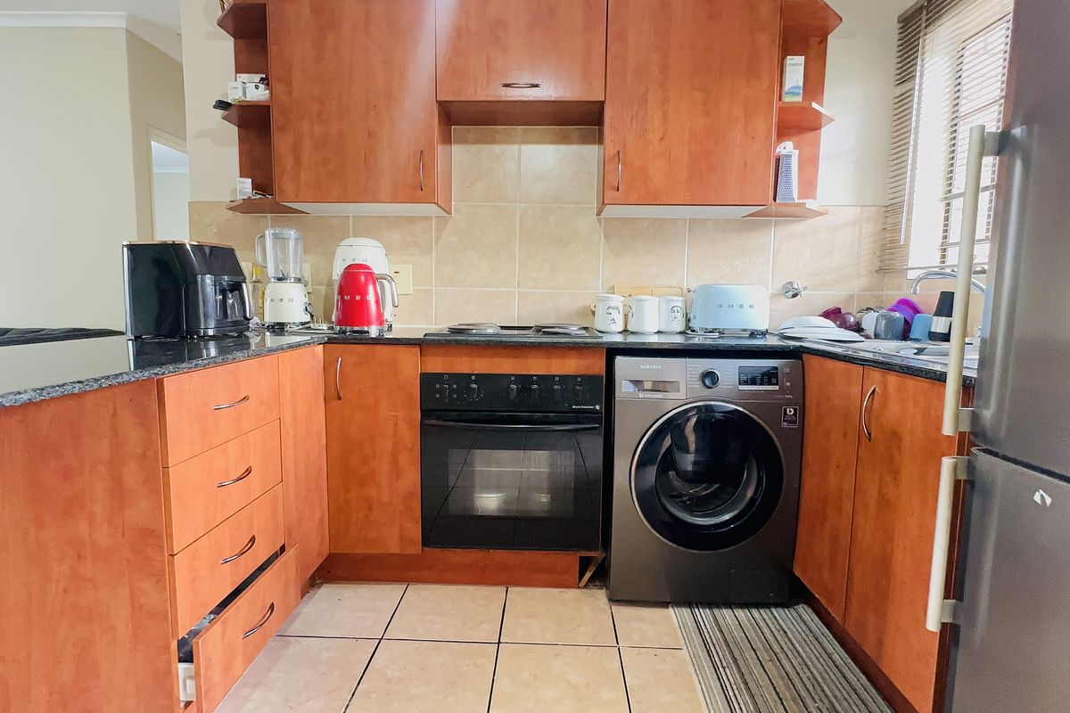 A functional kitchen featuring wood-finish cabinetry, granite countertops, a tiled backsplash, and integrated appliances including an oven, hob, and washing machine.