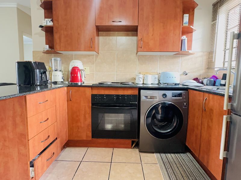 A functional kitchen featuring wood-finish cabinetry, granite countertops, a tiled backsplash, and integrated appliances including an oven, hob, and washing machine.