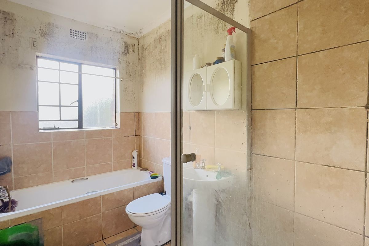 A dated bathroom featuring a bathtub, pedestal basin, and shower enclosure, currently requiring significant wall repairs and cosmetic renovation.