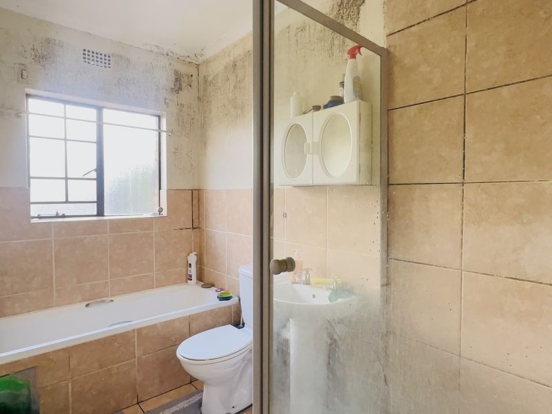 A dated bathroom featuring a bathtub, pedestal basin, and shower enclosure, currently requiring significant wall repairs and cosmetic renovation.
