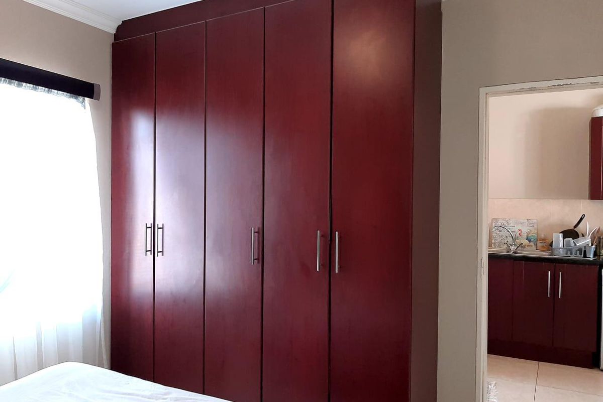 A bedroom featuring a large, dark wood built-in wardrobe with modern handles, with a view into an adjacent kitchen area.