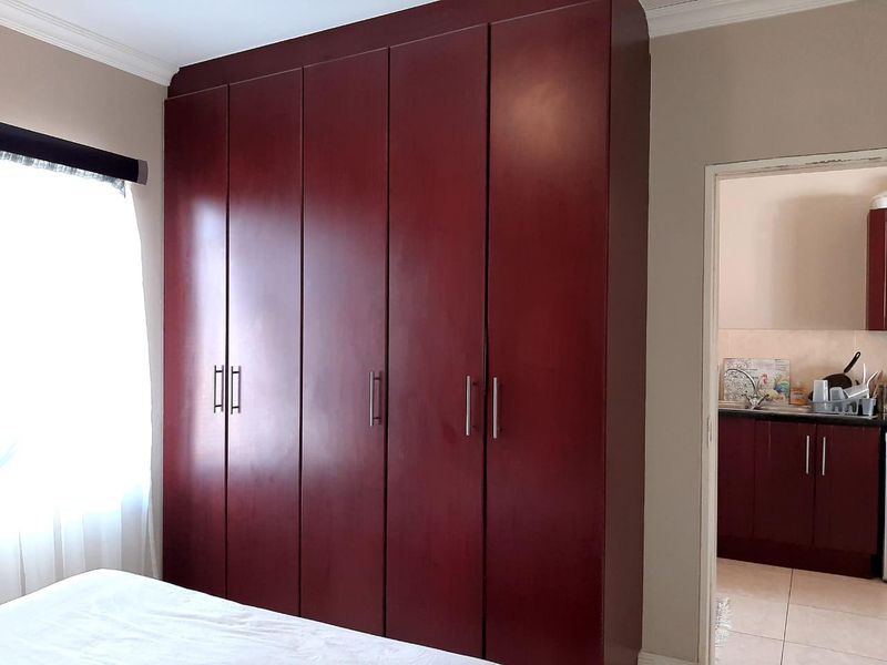 A bedroom featuring a large, dark wood built-in wardrobe with modern handles, with a view into an adjacent kitchen area.