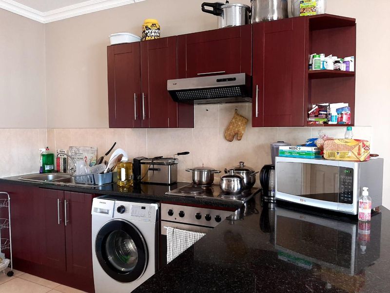 A functional kitchen featuring dark wood cabinetry, granite countertops, a built-in oven with hob, extractor fan, and an integrated washing machine.