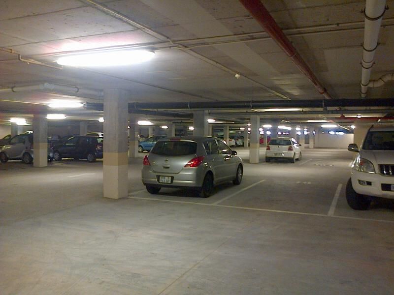 A functional underground parking garage featuring concrete flooring, structural columns, and exposed overhead utility piping.