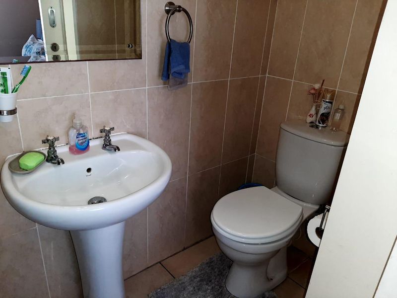 A functional bathroom featuring a pedestal basin, dual-flush toilet, and neutral ceramic wall and floor tiling.