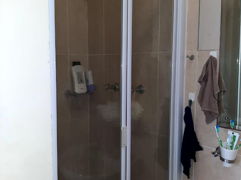 A functional bathroom featuring a tiled shower enclosure with a glass door, a pedestal basin, and a wall-mounted mirror.