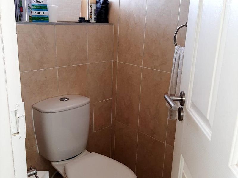 A compact bathroom featuring neutral wall and floor tiles, a standard toilet, and a wall-mounted towel ring.