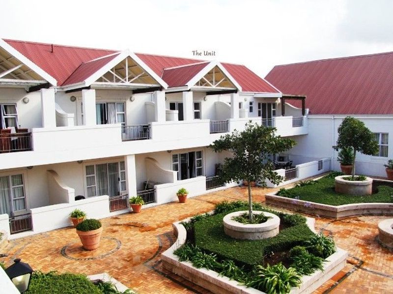 A view of the apartment complex courtyard featuring brick paving, raised garden beds, and balconies with metal railings under a red metal roof.