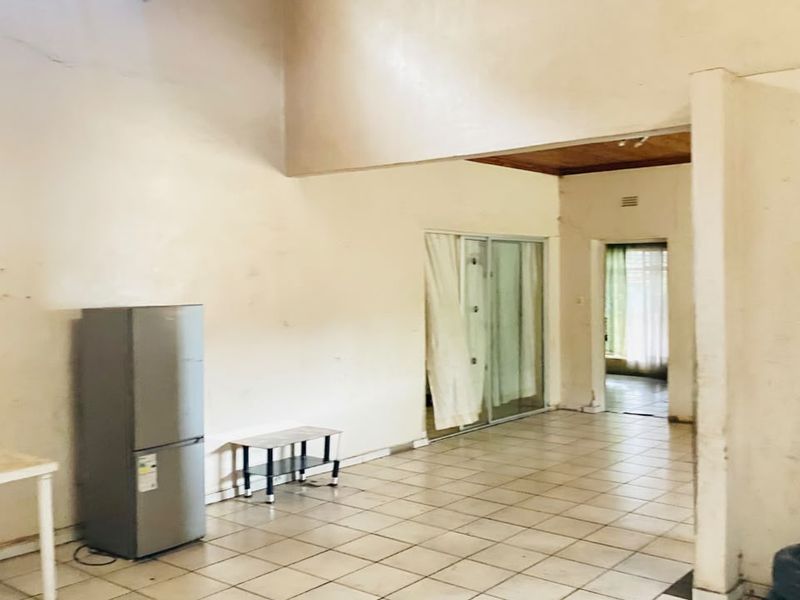 An open-plan living area featuring tiled flooring, sliding glass doors, and high ceilings, requiring cosmetic updates and wall repairs.