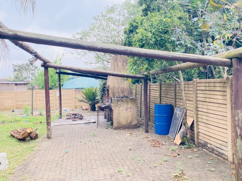 Outdoor patio area featuring a timber pergola structure and a built-in braai, set within a garden space with precast boundary walling.