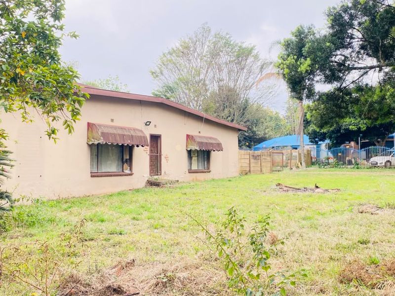 Rear view of the property featuring a large garden area and a single-story building with metal window awnings and a security entrance.