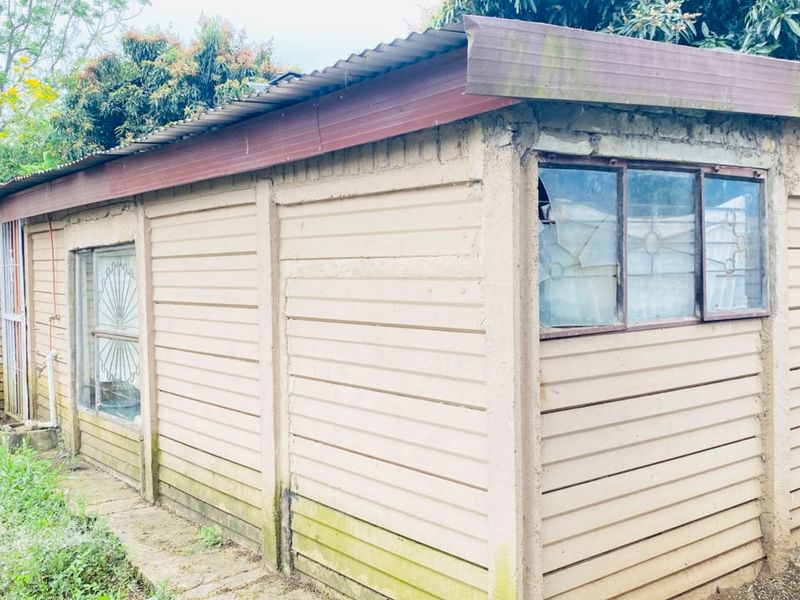 Exterior view of a detached outbuilding featuring precast concrete walling, a corrugated metal roof, and steel-framed windows with visible damage.