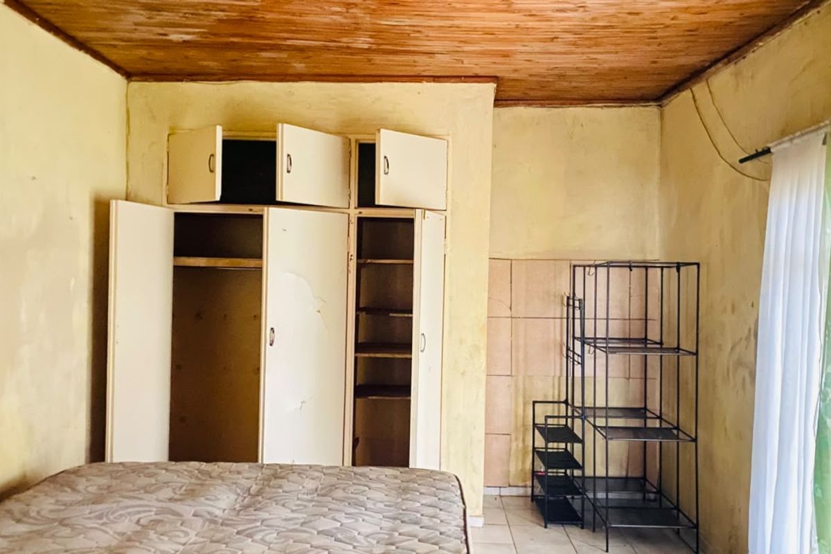 Bedroom featuring built-in cupboards, wooden ceiling, and tiled flooring. The room requires cosmetic updates and repairs to wall finishes and cabinetry.