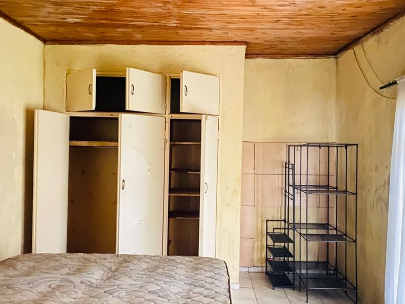 Bedroom featuring built-in cupboards, wooden ceiling, and tiled flooring. The room requires cosmetic updates and repairs to wall finishes and cabinetry.