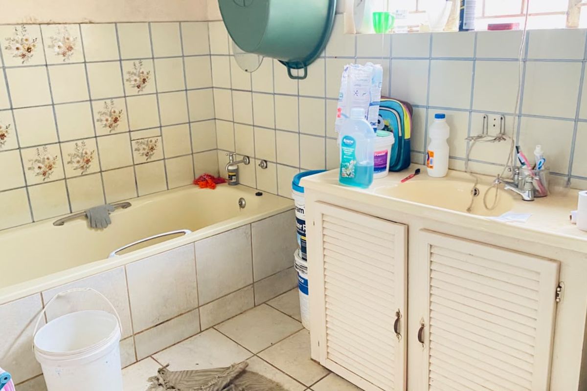 A dated bathroom featuring a built-in bathtub, vanity cabinet with basin, and original ceramic tiling, offering significant potential for modernization and renovation.
