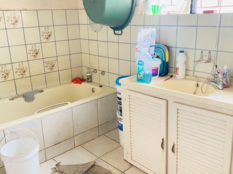 A dated bathroom featuring a built-in bathtub, vanity cabinet with basin, and original ceramic tiling, offering significant potential for modernization and renovation.