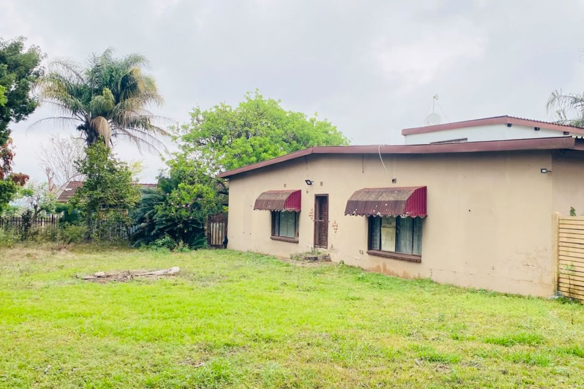 Rear view of the property featuring a large lawn area, weathered exterior walls, and metal window awnings.