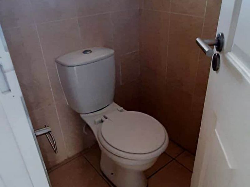 A compact bathroom featuring tiled walls and flooring, equipped with a standard toilet and a window for natural light.
