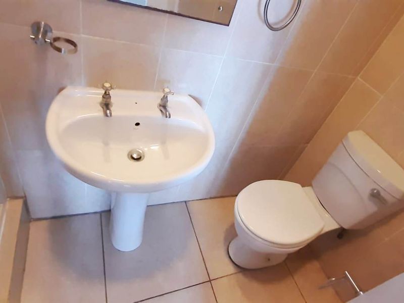 A functional bathroom featuring a pedestal washbasin, toilet, and shower enclosure with neutral wall and floor tiling.