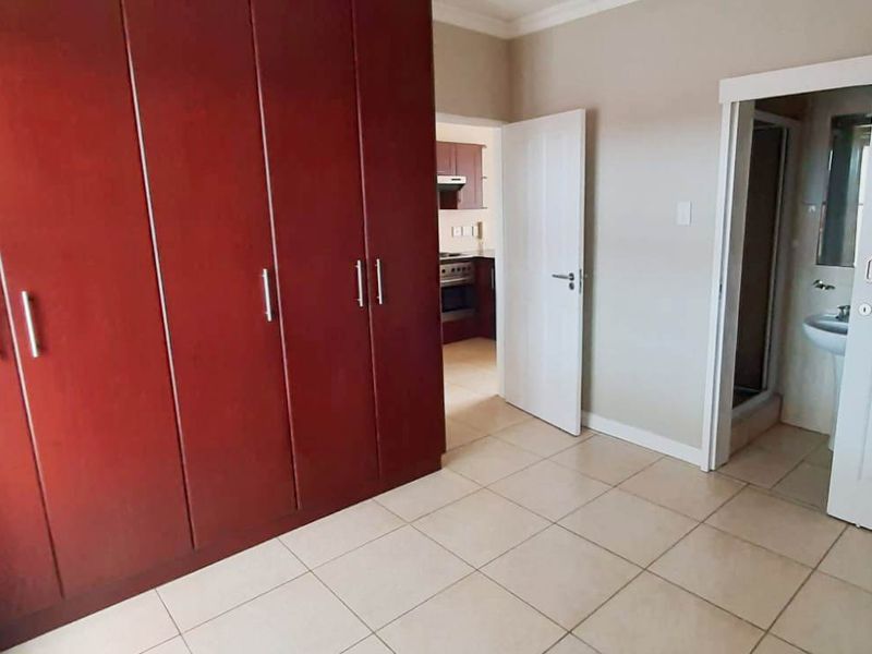 A spacious bedroom featuring large built-in wooden cupboards, neutral tiled flooring, and direct access to an en-suite bathroom.