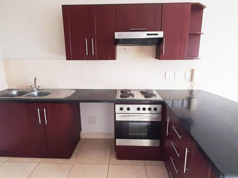 A clean, functional kitchen featuring dark wood cabinetry, black granite countertops, and integrated stainless steel appliances including an oven and extractor fan.