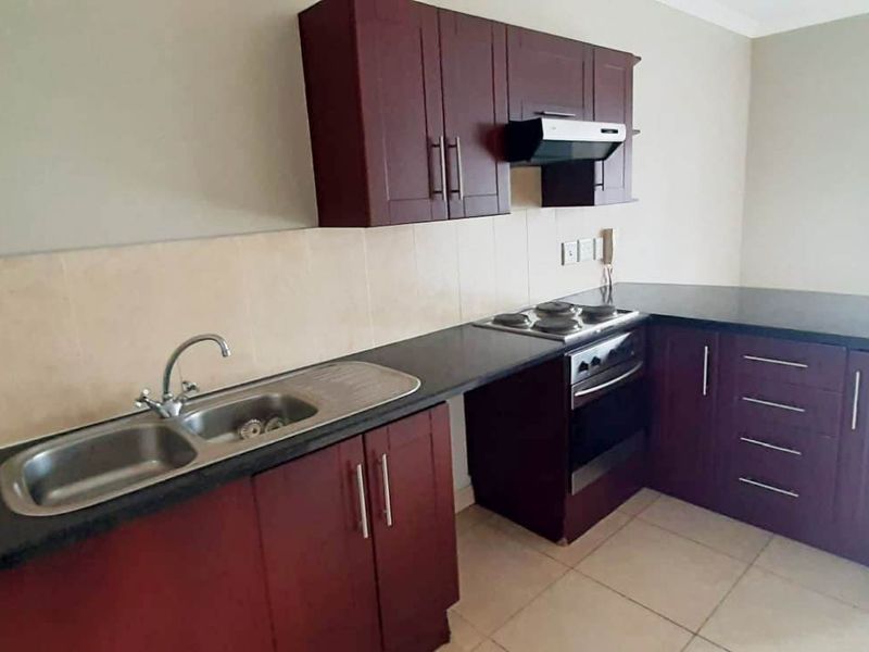 A functional kitchen featuring dark wood cabinetry, black granite countertops, a stainless steel double sink, and built-in cooking appliances with tiled flooring.