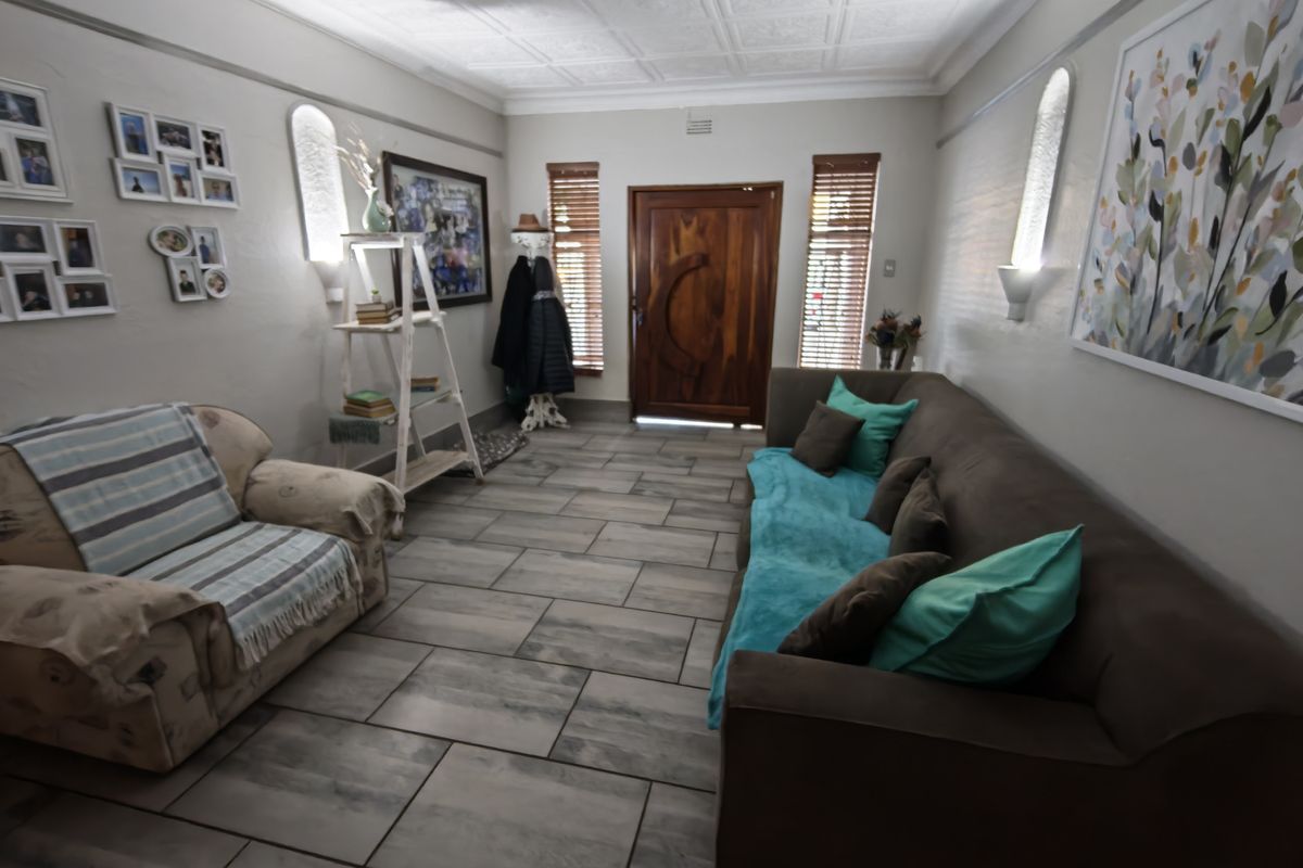 A well-maintained living room featuring tiled flooring, a decorative coffered ceiling, and a solid timber front entrance door with integrated wall lighting.