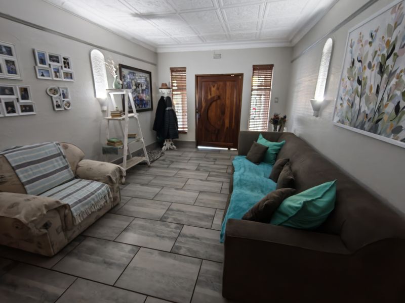 A well-maintained living room featuring tiled flooring, a decorative coffered ceiling, and a solid timber front entrance door with integrated wall lighting.