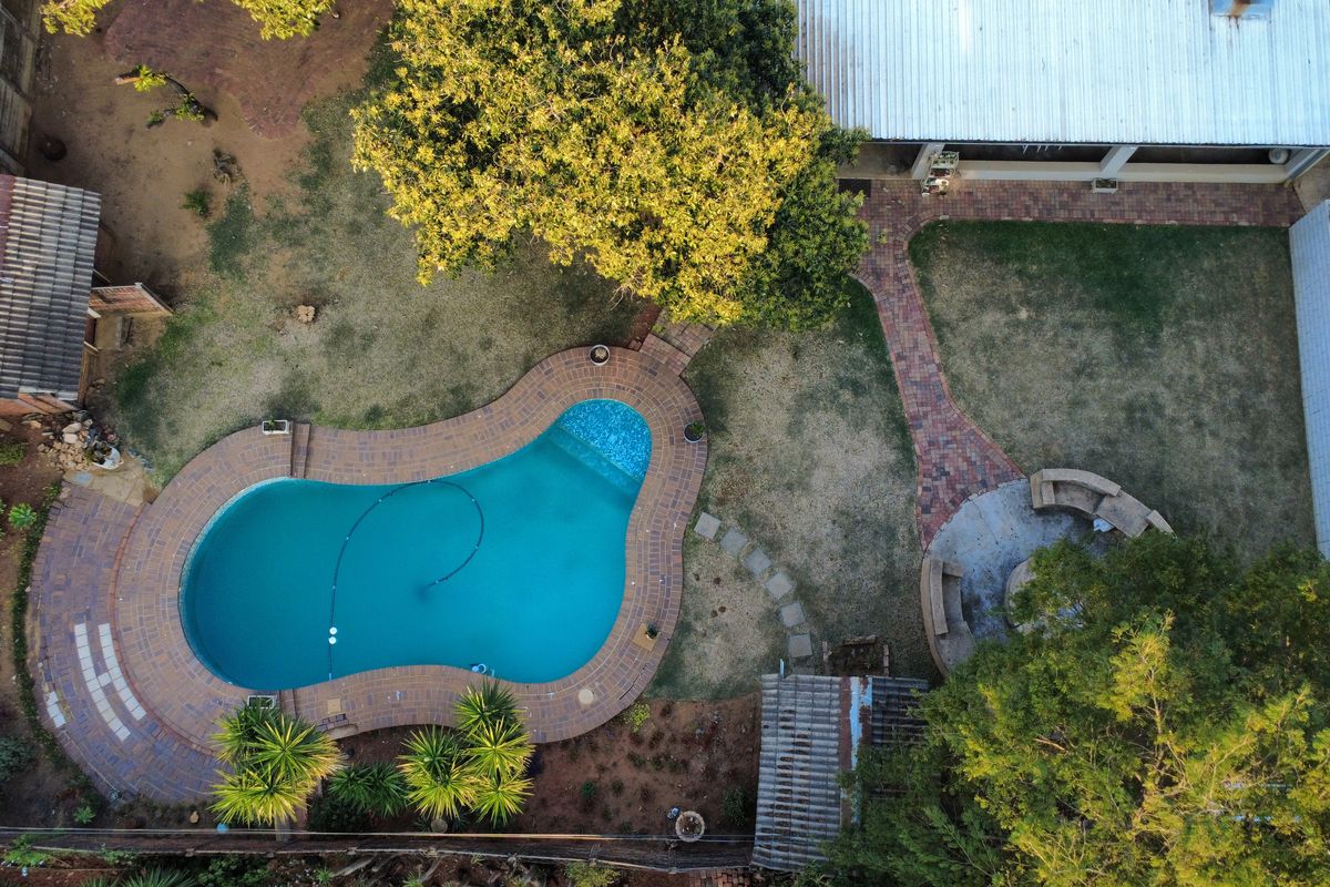 Aerial view of the backyard featuring a kidney-shaped swimming pool, brick paved pathways, built-in seating area, and established garden landscaping.