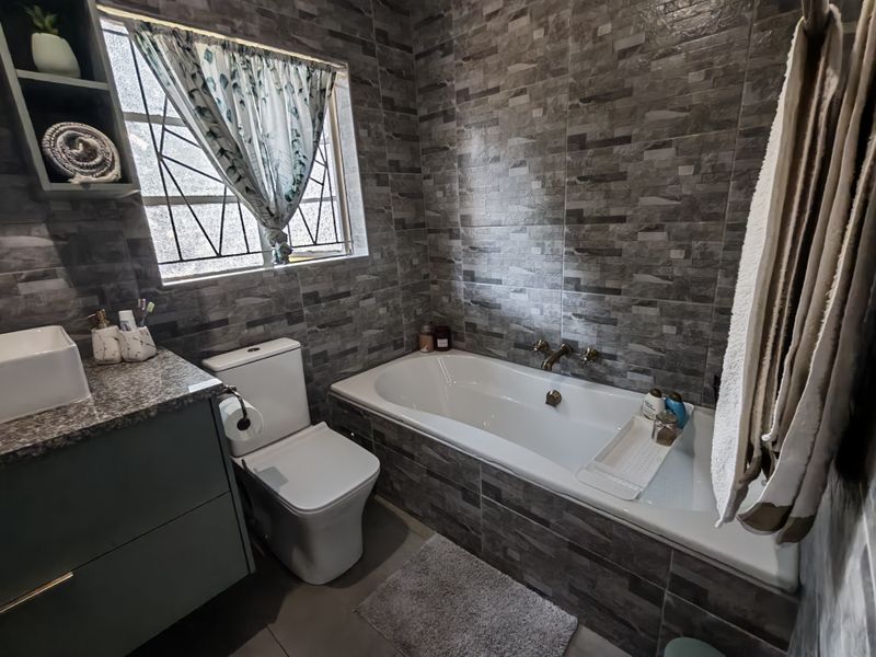A modern bathroom featuring a built-in bathtub, vanity with stone countertop, vessel sink, and contemporary grey tiled wall finishes.