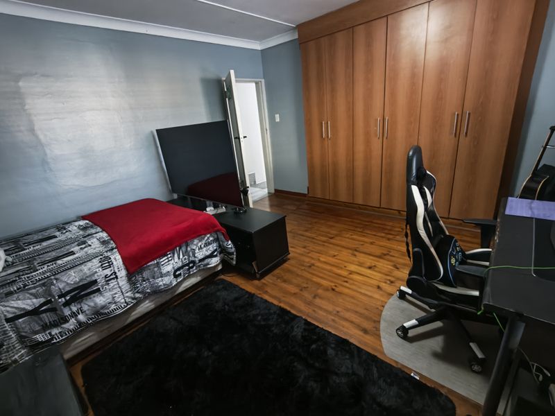 A bedroom featuring polished timber flooring, a large built-in wooden wardrobe, and coved ceiling details.