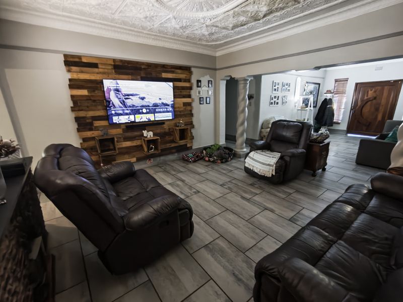 Spacious living room featuring a decorative pressed metal ceiling, timber feature wall, and modern tiled flooring, creating a warm and inviting atmosphere.