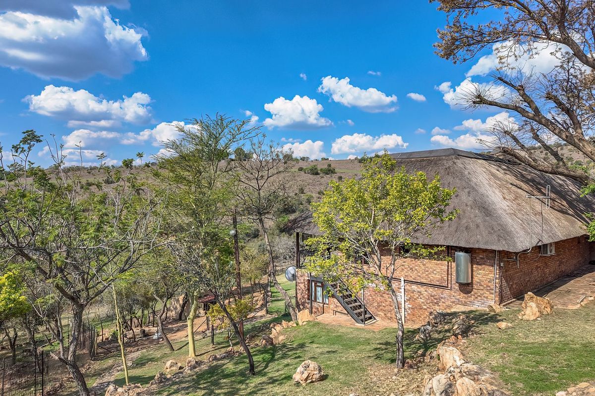 Rear view of a face brick house featuring a traditional thatch roof, external staircase, and surrounding natural landscape.